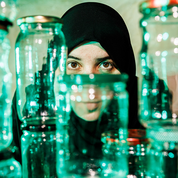 a woman in a black head scarf behind a collection of glass jars
