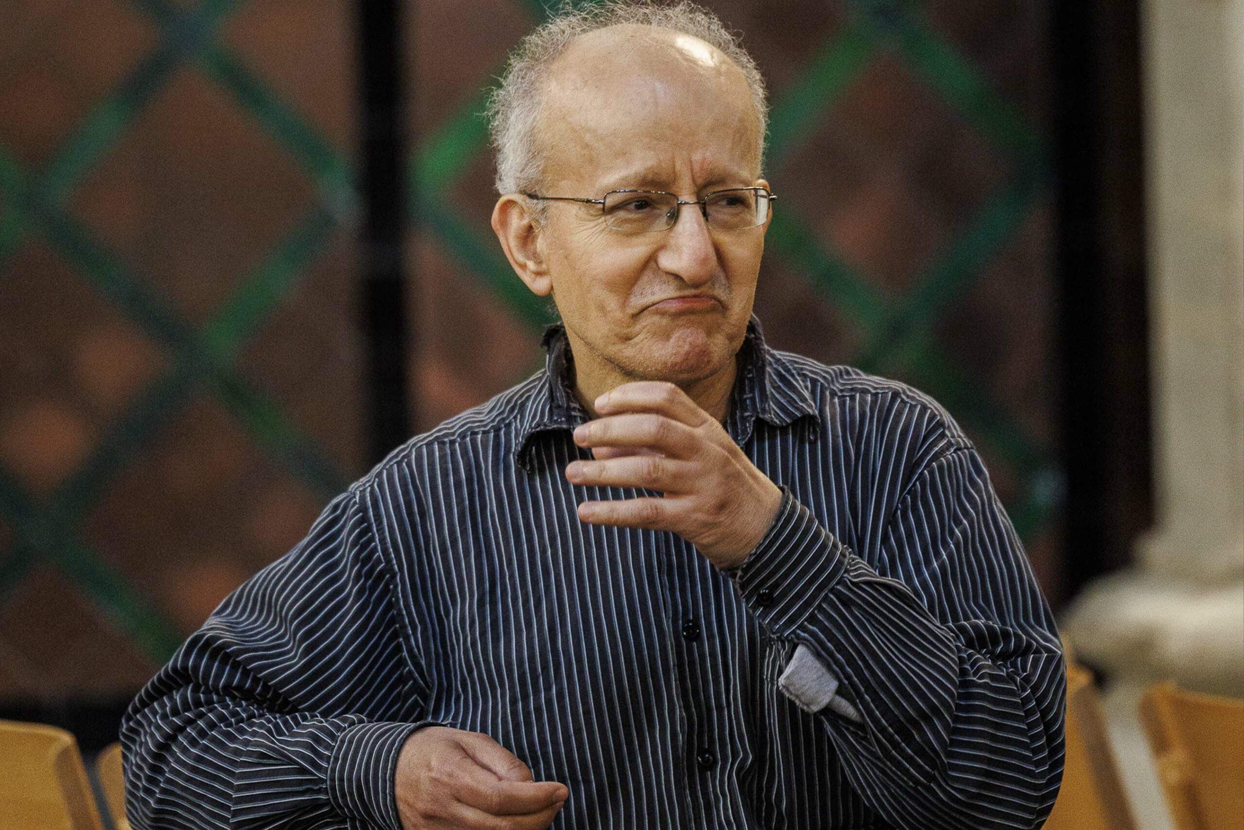 An elderly man wearing glasses and a striped shirt
